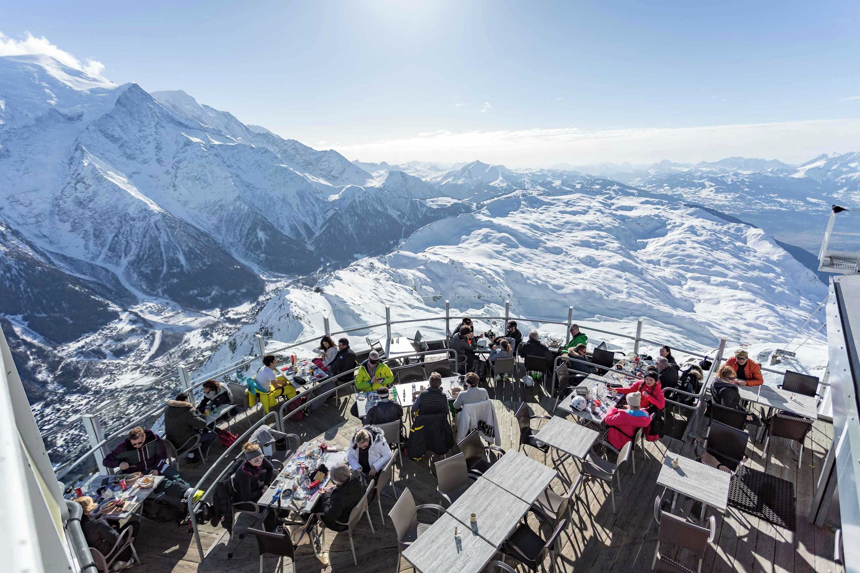 Restaurante em altitude com mesas ao ar livre e vista para uma paisagem nevada de montanhas.