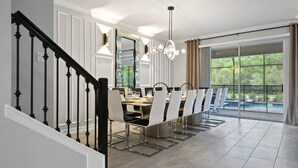 A dining area with a long table, chairs, a chandelier, and a staircase.