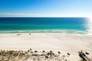 A beach with clear turquoise water, a sandy shore, and a few umbrellas.