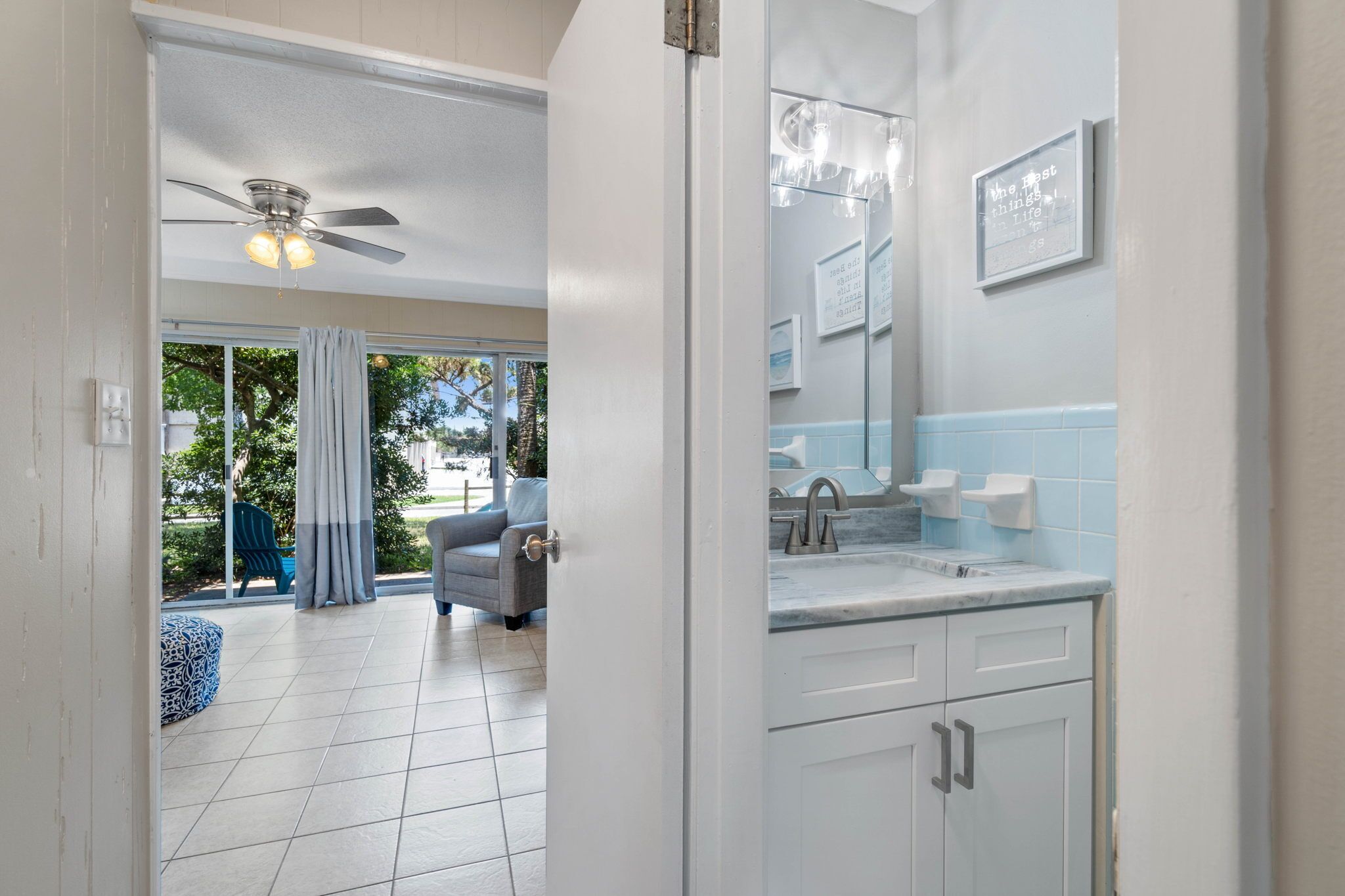 A modern bathroom with a large mirror, white cabinets, and a ceiling fan.