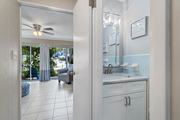 A modern bathroom with a large mirror, white cabinets, and a ceiling fan.