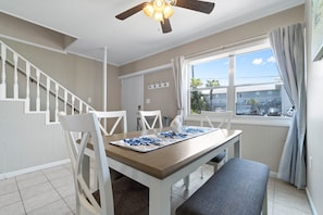 A dining area with a table, chairs, a ceiling fan, and a window with curtains.
