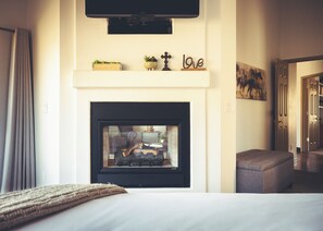 Une chambre d’hôtel avec une cheminée, un lit, un téléviseur fixé au-dessus de la cheminée et un couloir menant à une autre pièce.