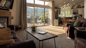 Amplia sala de estar con un gran ventanal corredero que da a un balcón, chimenea y área de cocina con electrodomésticos modernos.
