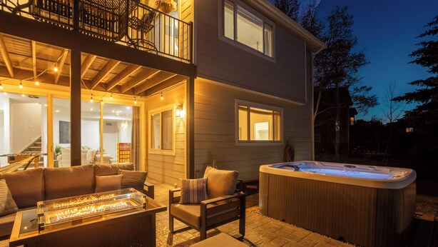Casa de dos pisos con jacuzzi, mobiliario exterior y balcón con luces de cuerda.