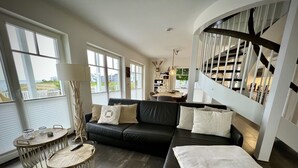 Ein modernes Wohnzimmer mit einer schwarzen Ledersofa, einem runden Holztisch und einer Treppe mit Geländer.
