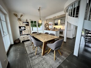 A modern kitchen with white cabinets, a wooden dining table, and a large island. - Holiday Home 'Sliminde by Seeblick Ferien ORO' with Sea View, Sauna & Wi-Fi (Kappeln)
