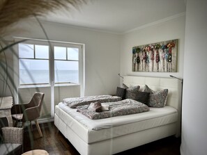 A bedroom with a bed, a window, a chair, a painting, and a lamp. - Holiday Home 'Sliminde by Seeblick Ferien ORO' with Sea View, Sauna & Wi-Fi (Kappeln)