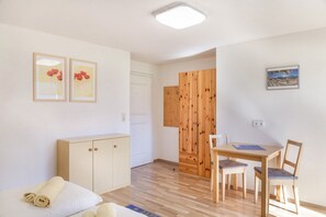 A room with a wooden dining table, chairs, a sofa, and a cabinet. There are two framed pictures on the wall.