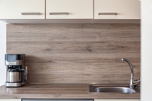 A kitchen with a built-in coffee maker, a stainless steel sink, and wooden panel backsplash.