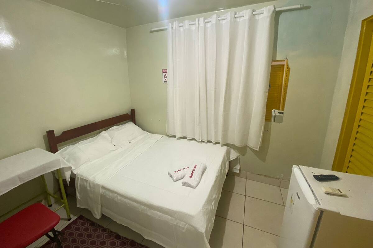 Una habitación pequeña y limpia con una cama individual, un escritorio y un refrigerador pequeño.