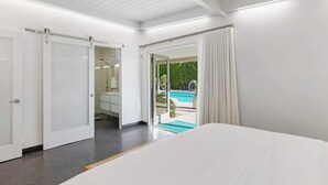 A bedroom with a bed, a bathroom with a mirror, and a sliding glass door leading to a pool. - Sunset Glamour - Enchanting Luxury Zen Retreat (Palm Springs)