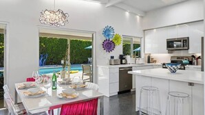 A modern kitchen with white cabinetry, a built-in microwave, and a large island with bar stools. - Sunset Glamour - Enchanting Luxury Zen Retreat (Palm Springs)