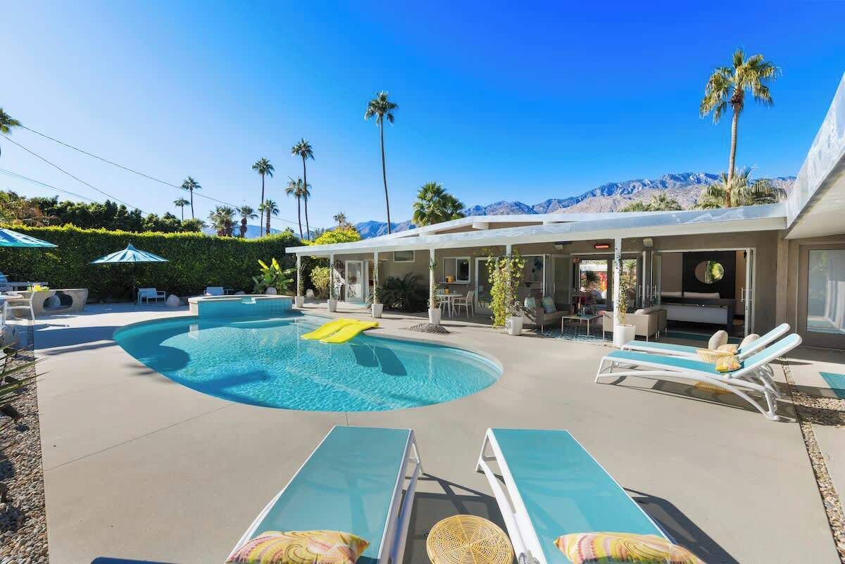 A pool area with lounge chairs, a covered patio, and a mountain backdrop.