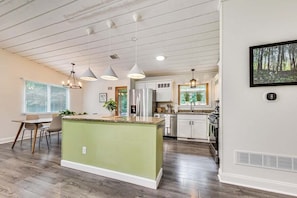 A modern kitchen with a central island, pendant lighting, and a dining area with chairs.
