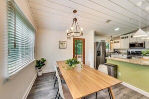A modern kitchen with a wooden dining table, a chandelier, and a view to the outside.