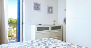 Quarto com cama, cômoda, duas obras de arte na parede e varanda com vista.