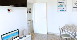 Une pièce comprenant un lit, un bureau avec un ordinateur, une chaise, une table recouverte d’une nappe à carreaux et des œuvres d’art représentant des poissons accrochées au mur.