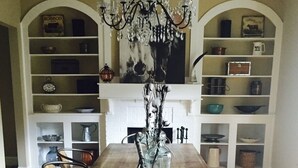 Comedor con mesa de madera, sillas, candelabro y estanterías con utensilios de cocina.
