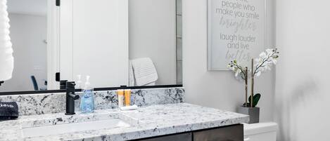 A bathroom with a marble countertop, a sink, a mirror, a toilet, and a wall-mounted sign with a motivational quote.