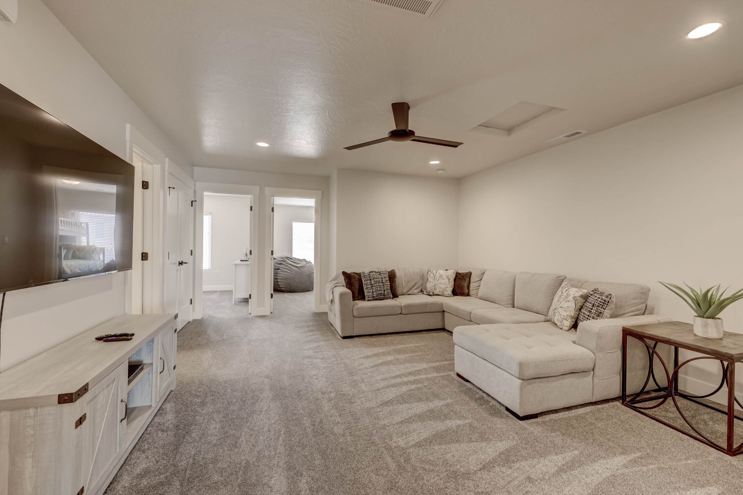 A spacious living room with a sectional sofa, a flat-screen TV, and a ceiling fan.