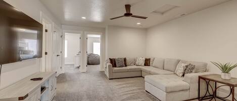 A spacious living room with a sectional sofa, a flat-screen TV, and a ceiling fan.