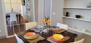 Una mesa de comedor dispuesta con platos coloridos y copas de vino, un florero con flores y una partición de espejo.