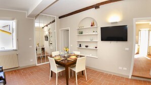 Un comedor con mesa de madera, sillas blancas y televisor montado en la pared.