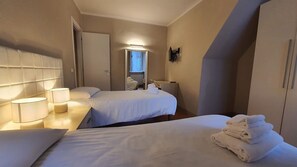 Habitación de hotel con dos camas, un escritorio y una silla. Una ventana deja entrar luz natural.