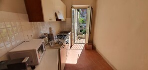 Cocina compacta con microondas, estufa y pileta, que da a un balcón con vistas al exterior.