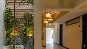 A hotel corridor with a tiled floor, a wooden wall with plants, and a ceiling with hanging lamps. - Loft 101 - w/balcony - Daily Cleaning (Santo Domingo)