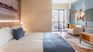 A hotel room with a large bed, a desk, a chair, and a view of the city through the window. - Loft 101 - w/balcony - Daily Cleaning (Santo Domingo)