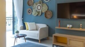 A modern living room with a sofa, a small round table, a flat-screen TV mounted on the wall, and a wooden console table. - Loft 101 - w/balcony - Daily Cleaning (Santo Domingo)