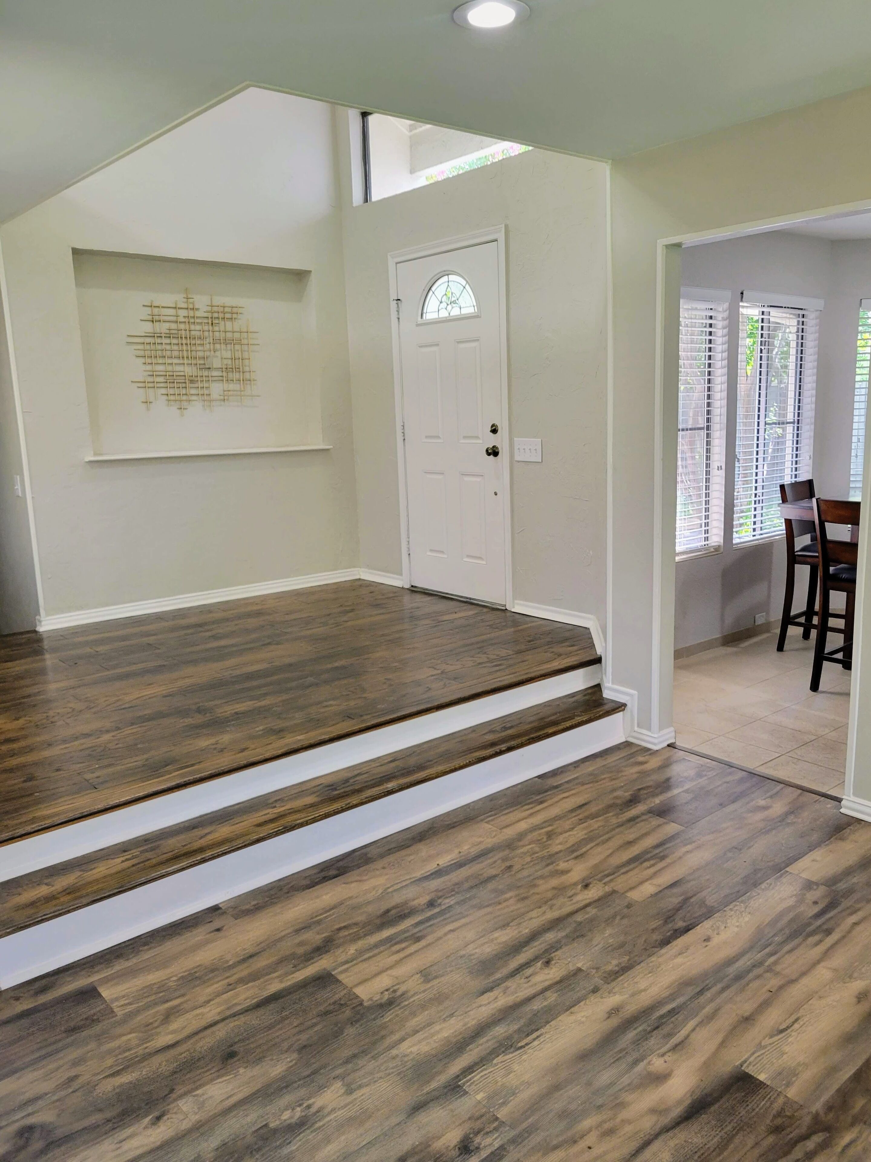Une pièce dotée d’un plancher en bois, d’une porte blanche avec un panneau de verre et d’un escalier menant à un autre espace.