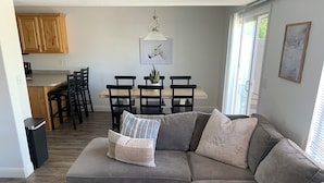 A living room with a grey sectional sofa, a dining area with a wooden table and chairs, and a kitchen with wooden cabinets. - Cozy Townhome Gathering Spot (Clinton)