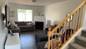 A living room with a sofa, ottoman, white side table, and a staircase. - Cozy Townhome Gathering Spot (Clinton)