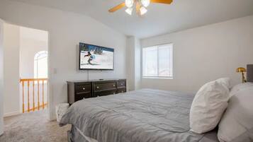 A bedroom with a bed, a ceiling fan, a TV, a window, and a door leading to another room.