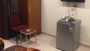 A room with a wooden wardrobe, a red chair, a small table, a television mounted on the wall, and a grey cabinet with electronic devices. - Blue Eyes Hotel (Giza)