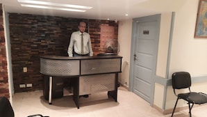 A reception desk with a man standing behind it, a wall clock, and a door with a number plate. - Blue Eyes Hotel (Giza)