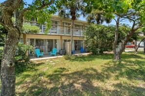 A two-story building with a balcony, outdoor seating area with chairs, and a tree in the foreground. - 2 bedroom Newly remodeled, walk to the Beach! Sleeps 6 (Fort Walton Beach)
