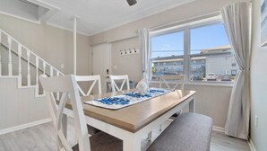 Un comedor con mesa, sillas, un banco, un ventilador de techo y una ventana con cortinas.