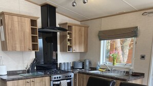 Una cocina compacta con armarios de madera, una estufa y un comedor preparado para cuatro, con mesa, sillas y vajilla.