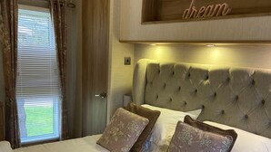 Una cama bien hecha con almohadillas de estampado floral y un cabecero, una ventana con cortinas y un estante de madera con la palabra 'dream'.
