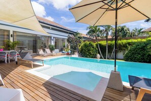 A swimming pool with a wooden deck, lounge chairs, and a covered area with an umbrella.