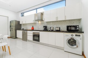 A modern kitchen with white cabinetry, a stainless steel refrigerator, a built-in oven, a microwave, a coffee maker, and a washing machine.
