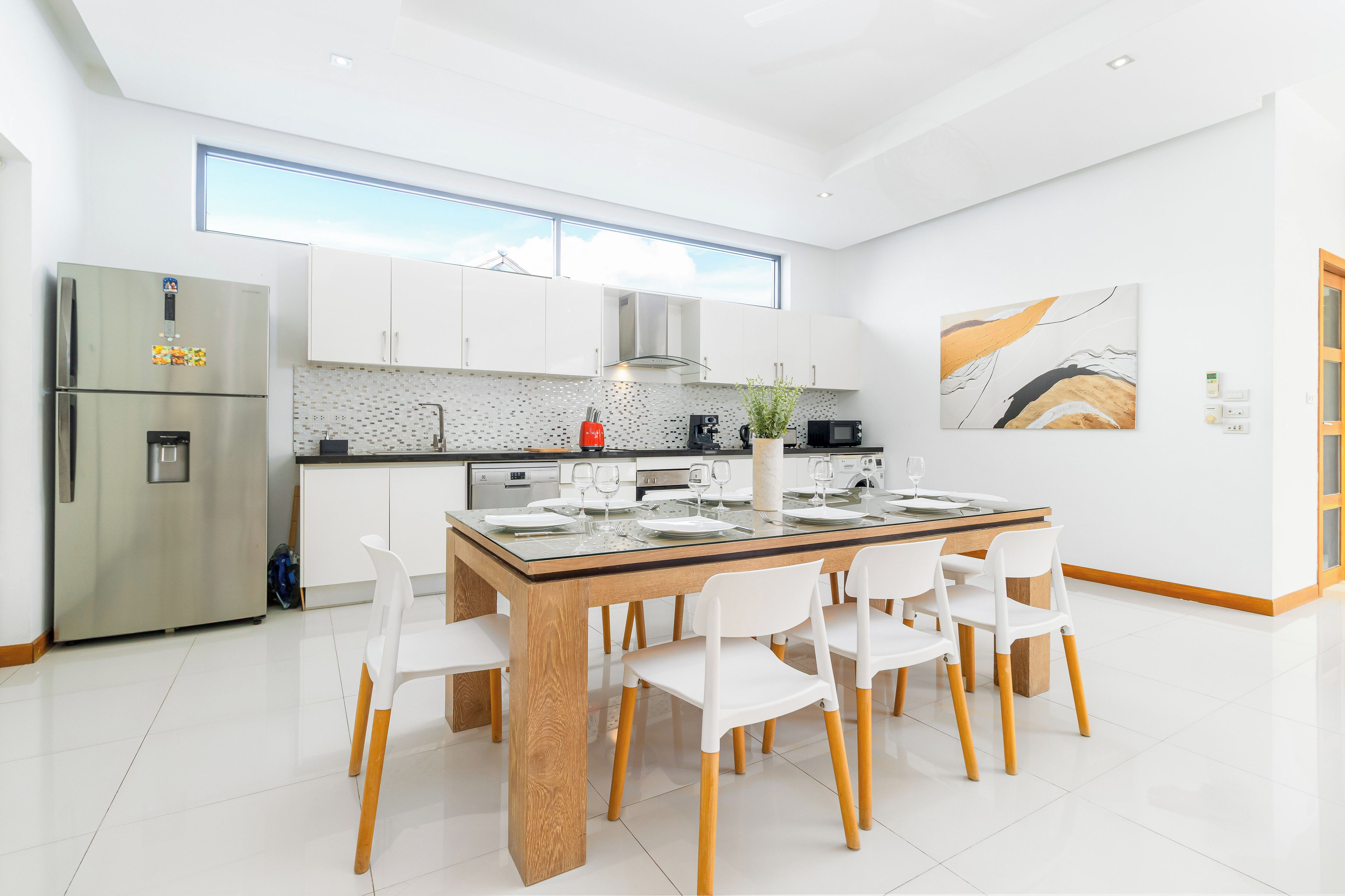 Cocina moderna con una isla central, muebles blancos y un refrigerador de acero inoxidable.