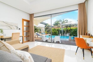 A modern living room with a large window, a pool, and outdoor seating.