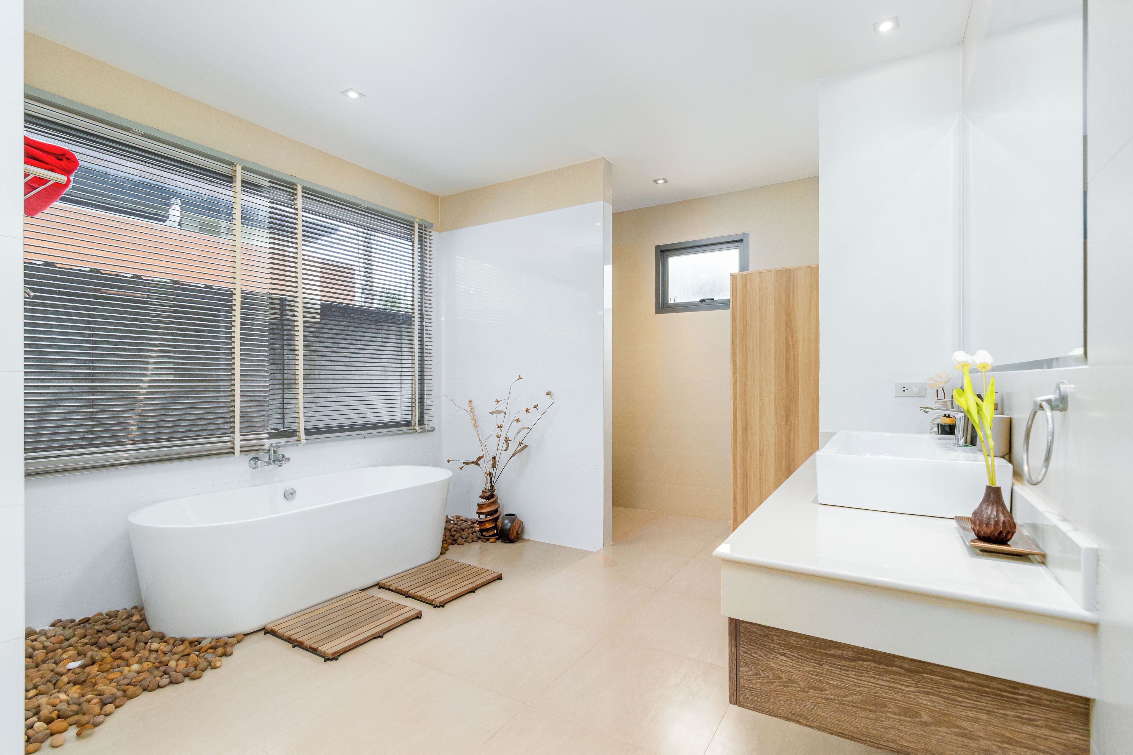A modern bathroom with a freestanding bathtub, a vanity with a mirror, and a window with blinds.
