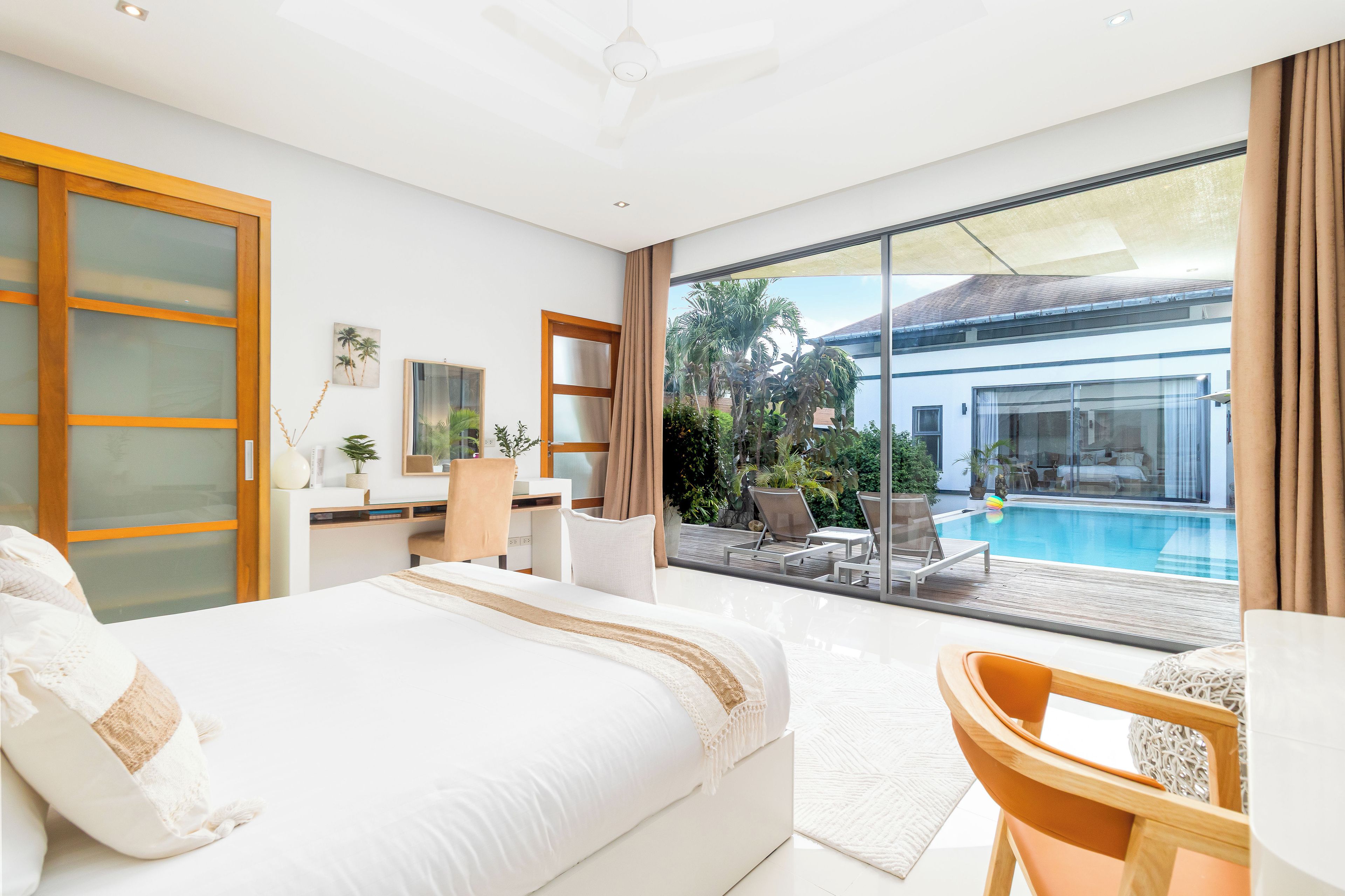 Una camera d'albergo con un letto grande, una scrivania, una sedia, vista su una piscina e un balcone.