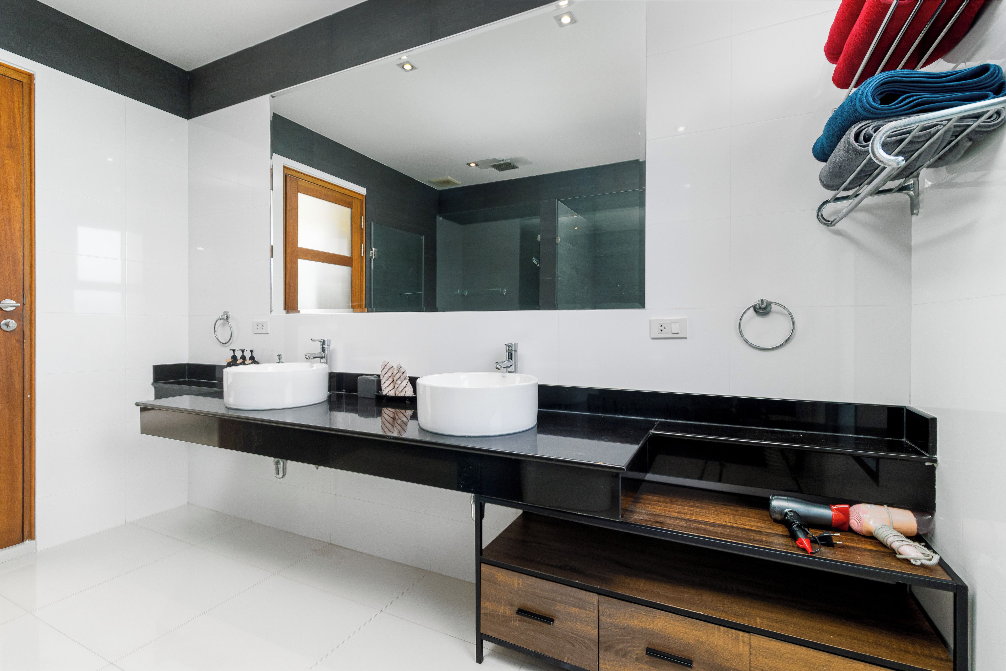 A modern bathroom with two sinks, a large mirror, and a towel rack.